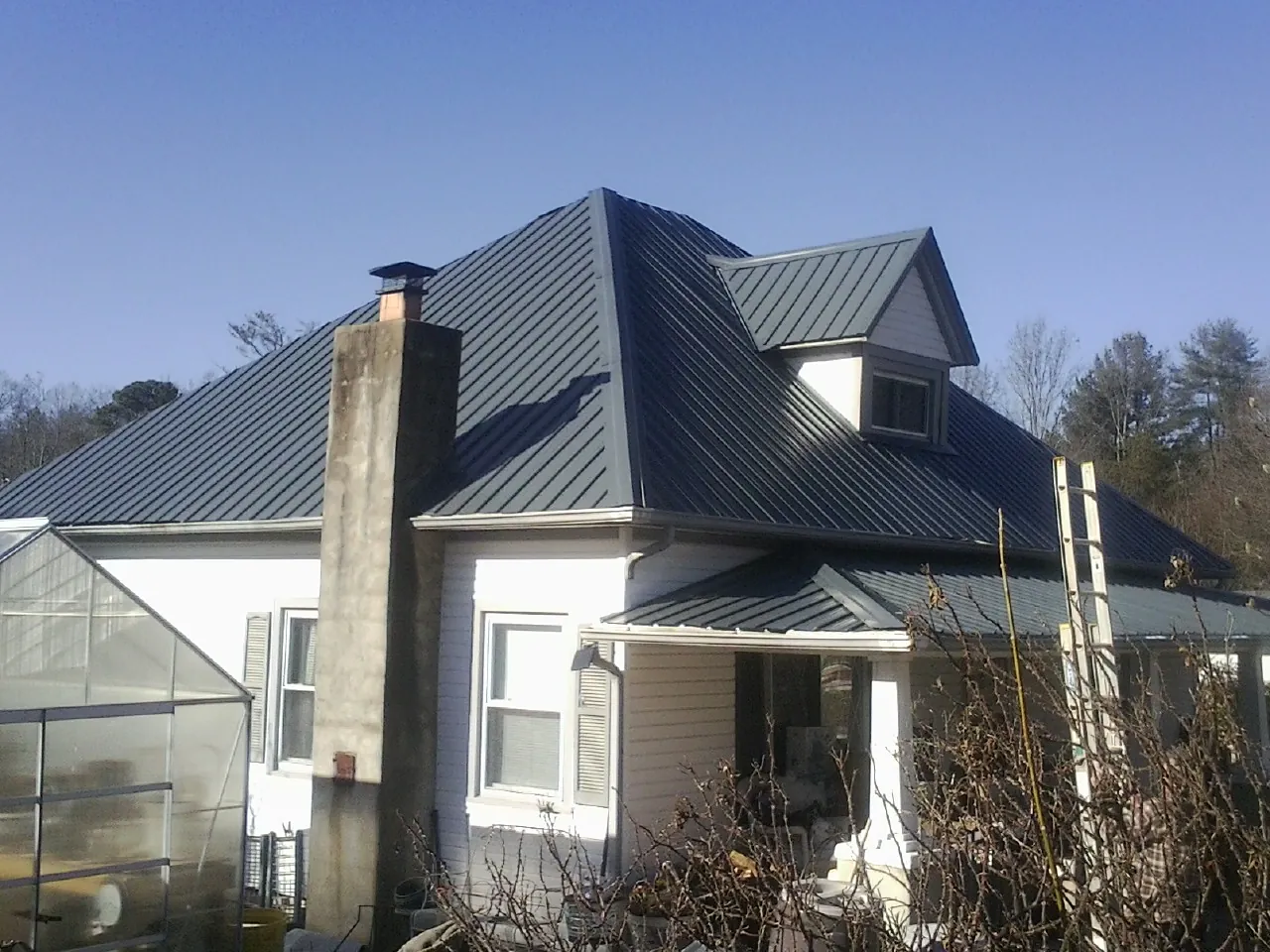 Dark blue standing seam metal roof on a white farmhouse with dormer — Slate & Tile Roof Repair by Roofing Brothers in Blakesburg