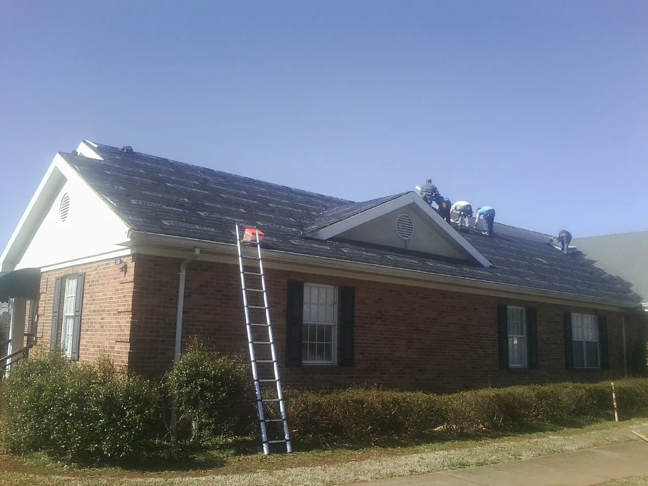 Crew tearing shingles off a brick ranch roof with a ladder set — Emergency Roof Repair work by our crew in Blakesburg