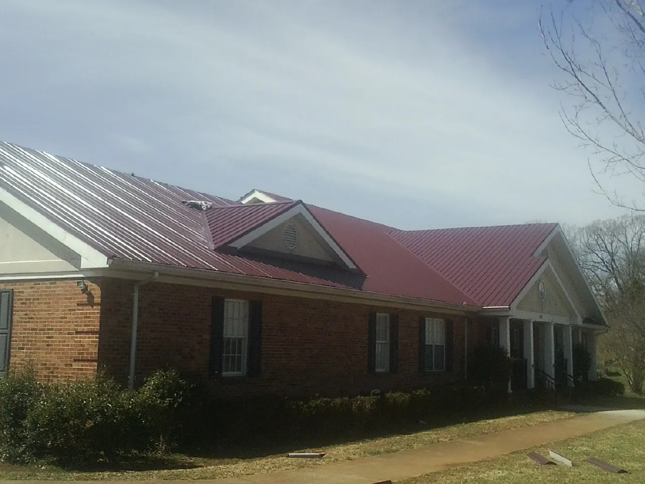 Red metal roof with gabled entries on a long brick building, from a Hail Damage Roof Repair job in Blakesburg
