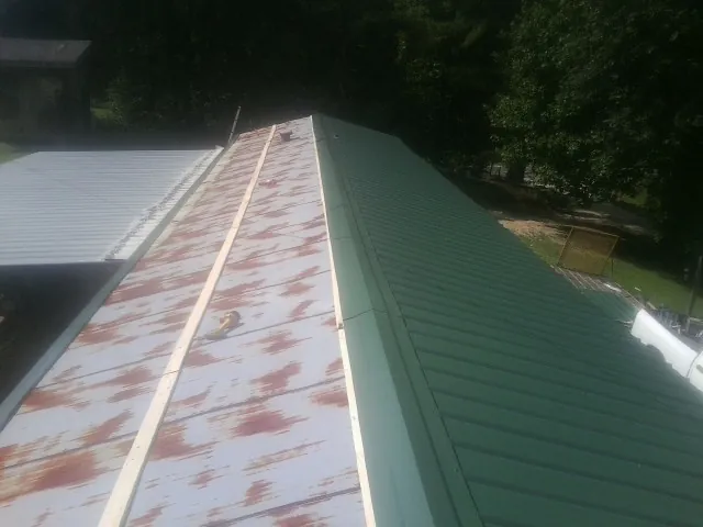 Old rusted panels beside newly installed green metal roofing — Wind Damage Roof Repair by Roofing Brothers in Blakesburg