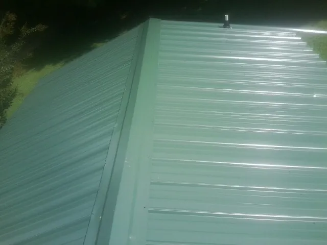 New green metal panels meeting at the ridge of a roof — Flat Roof Repair work by our crew in Blakesburg