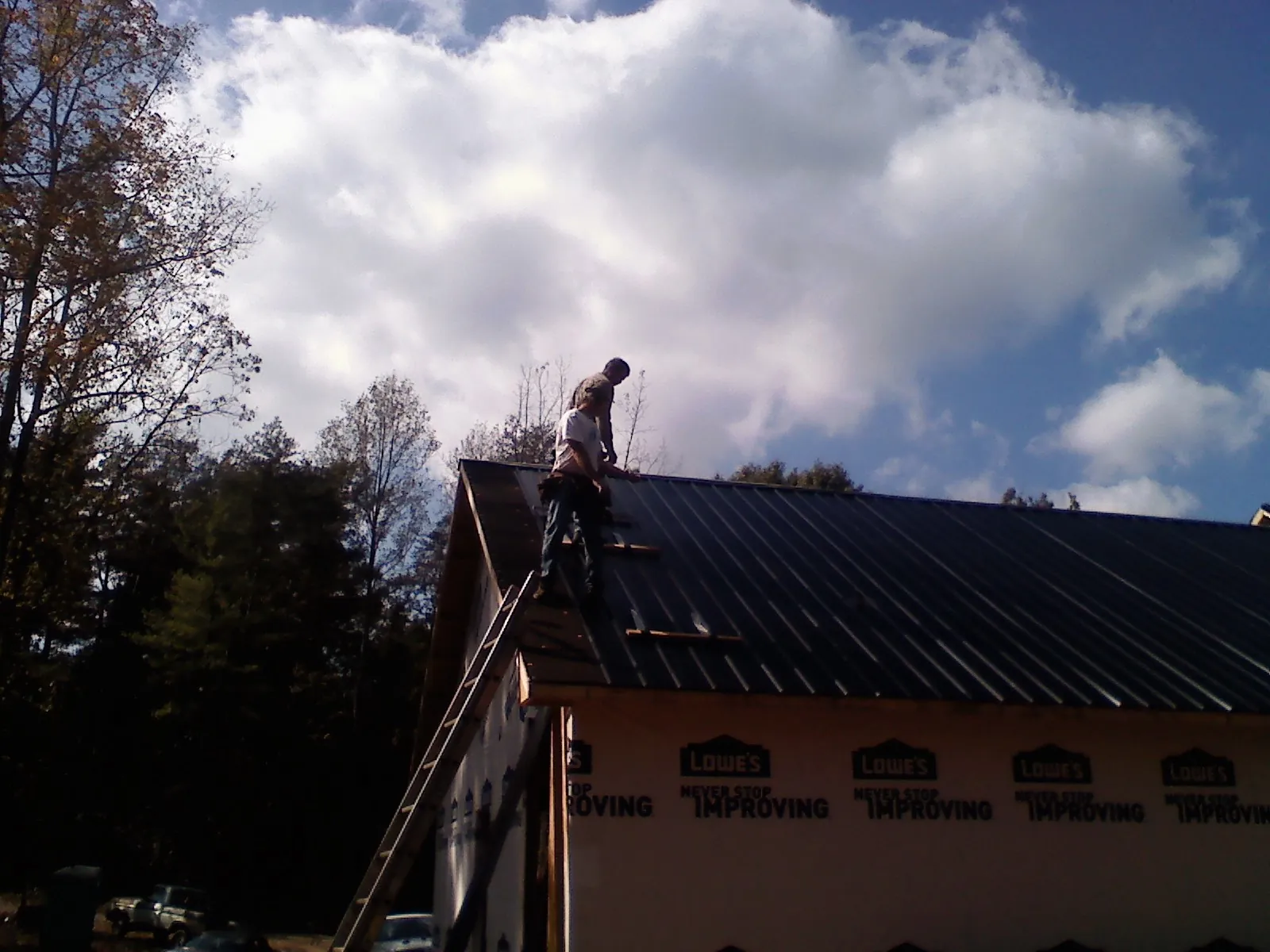 Roofer fastening dark metal panels high against a cloudy sky, from a Roof Inspection job in Blakesburg