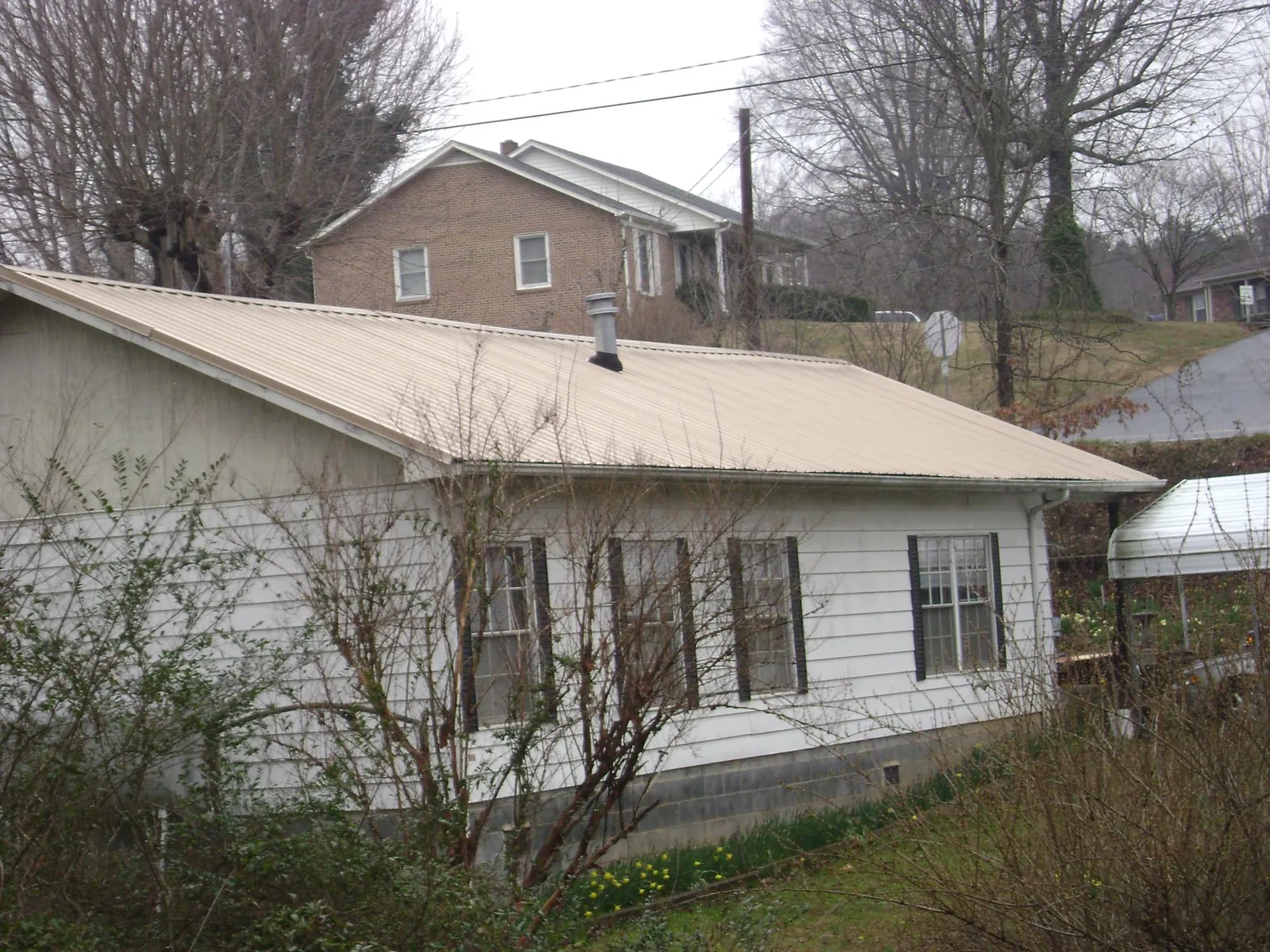 Tan metal roof on a white sided house set into a hillside — Commercial Roofing by Roofing Brothers in Blakesburg